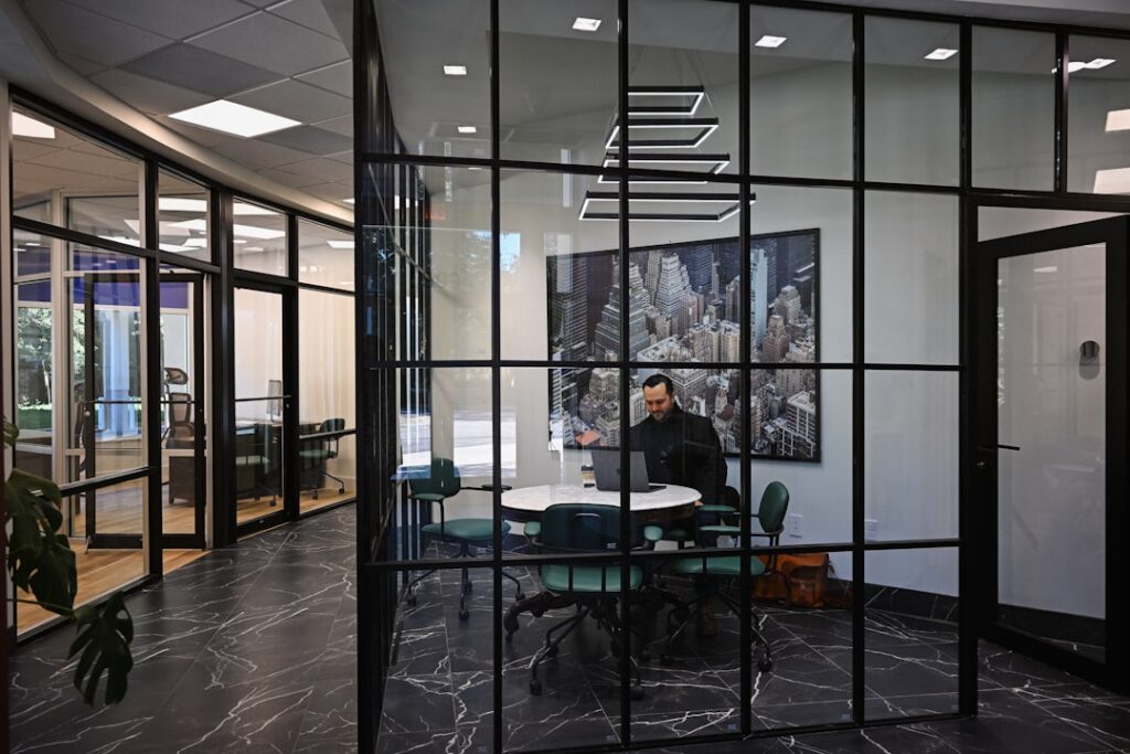 Confident and professional real estate agent stands in a bright, modern office, looking out at a city skyline, contemplati...